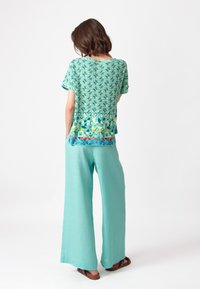Korte mouw top in teal met een geometrisch patroon; gecombineerd met losse, licht teal broeken. Lichtgewicht stof; relaxte pasvorm.