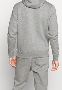 Felpa grigia con cappuccio e pantaloni tuta abbinati, realizzati in un morbido tessuto testurizzato. Presenta un cappuccio e polsini elasticizzati. Design semplice senza motivi visibili.