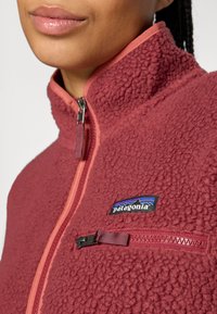 Detailní záběr na osobu, která má na sobě červenou fleecovou bundu Patagonia se zipem a náprsním zipem.