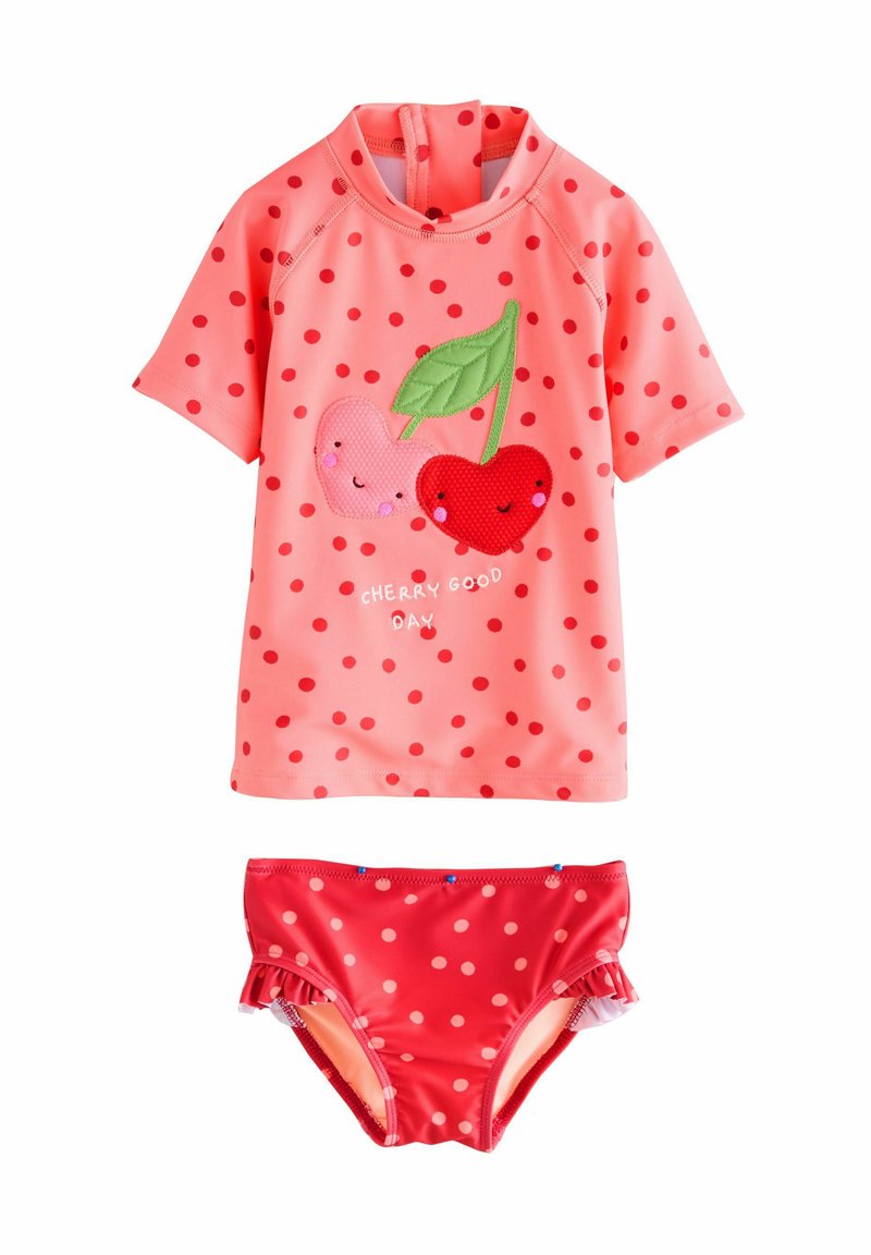 Ensemble de rash guard à manches courtes en rose, orné de pois rouges et d'appliqués cerise. Bas de bikini assortis à pois rouges.