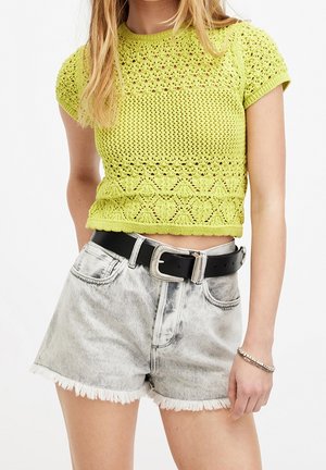 Mujer con top corto de crochet de color verde lima con mangas cortas y pantalones cortos de mezclilla gris claro de talle alto con cinturón negro y hebilla plateada.