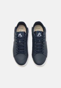 Navy leather sneakers with white rubber soles, round toe, and flat laces. Features logo on the tongue and side. Smooth texture.