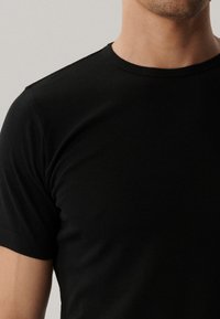 Czarny t-shirt z okrągłym dekoltem, charakteryzujący się miękką, gładką fakturą i krótkimi rękawami, ściśle dopasowany do ciała, bez widocznych wzorów czy akcentów.