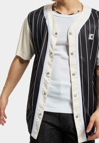 Camicia a righe nera e crema con maniche corte, dotata di un colletto rotondo e di un piccolo logo sul petto. Tessuto texture.