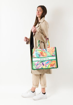 Borsa a spalla colorata con motivo floreale, dettagli verdi e branding. Il materiale sembra essere tessuto, con manici robusti per il trasporto.