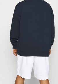 Granatowa bluza z długimi rękawami i luźnym krojem, zestawiona z białymi szortami. Bluza posiada prążkowany dekolt i dół.