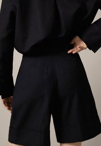 Marinblå shorts i skräddarsydd design, med två bakfickor, vikta fållar och en slät textur.