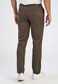 Bruine op maat gemaakte broeken met een gladde textuur, slim fit en twee achterzakken; gedragen met witte sneakers.