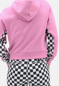 Sudadera rosa con capucha y mangas a cuadros en blanco y negro, combinada con pantalones a cuadros a juego que tienen bolsillos laterales.