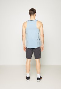 Camisa sin mangas azul claro con tejido texturizado y detalles en navy, combinada con pantalones cortos deportivos grises. El modelo se encuentra de espaldas.