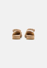 Tan suede sandals with adjustable ankle straps, low square heels, and a cushioned insole for comfort. Rear view showcases minimal design.