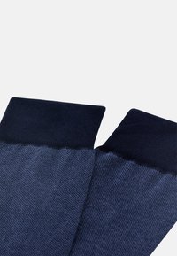 Tmavě modré ponožky s ribovaným horním okrajem a hladkou texturou. Tělo ponožek přechází z tmavších do světlejších odstínů.