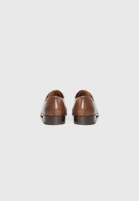 Chaussures en cuir marron avec une finition brillante, des orteils arrondis et un petit talon empilé. Elles présentent une texture lisse et peu d'accents décoratifs.