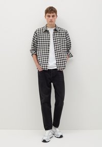 Chemise à carreaux noir et blanc sur un t-shirt blanc, associée à un jean noir et des chaussures de sport blanches. Design simple avec une coupe décontractée.