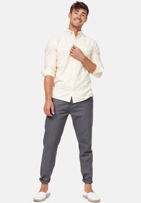 Camicia button-up gialla chiara con maniche lunghe, pantaloni grigi a sigaretta e scarpe bianche slip-on. Tessuto fresco e design semplice.