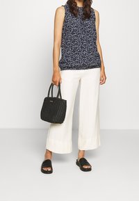 Marinblommig ärmlös topp, vita vida byxor, svart vävd handväska och svarta sjalettklackar. Slät tyg med subtila mönster och texturer.