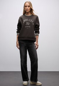 Ciemnoszary sweatshirt z białym tekstem, prążkowanymi mankietami i dołem. Połączony z czarnymi spodniami z szerokimi nogawkami i kremowymi sneakersami. Gładka tekstura.