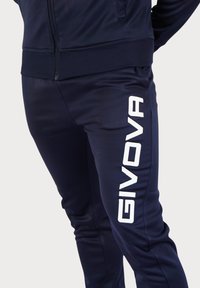 Modre trenirka hlače iz gladkega materiala z belim logotipom "GIVOVA", ki je natisnjen pokončno ob levi nogi. Prilegajoč dizajn in elastika v pasu.