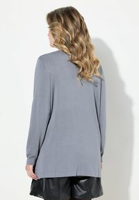 Haut gris à manches longues en tissu texturé, présentant une coupe décontractée, un col rond et des fentes latérales, associé à un short noir.