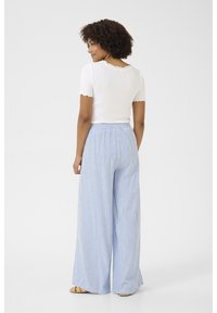 Bela rebrasta majica s kratkimi rokavi z valovitimi robovi in hlače z visokim pasom v modro-beli črtasti vzorec širokih nogavic. Vidni so ravni sandali.