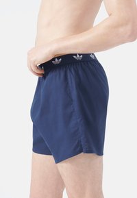 Pantaloni da bagno blu navy con una cintura elastica, caratterizzati da un motivo a logo ripetuto. Tessuto leggero con una vestibilità comoda e fessure laterali.