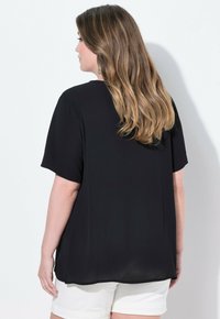 Maglietta nera a maniche corte con una vestibilità ampia, texture morbida e scollatura rotonda. Il retro presenta un orlo leggermente più lungo per una copertura aggiuntiva.