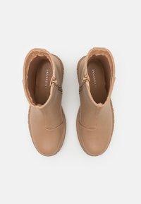 Botines tobilleros marrones con un acabado de cuero suave, paneles laterales elásticos y una suela de goma, con un cierre de cremallera para facilitar el uso.