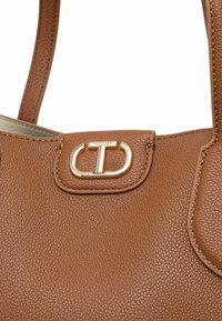 Borsa a mano in pelle di colore marrone con doppio manico e una fibbia in metallo dorato con il logo "CT" sul davanti.
