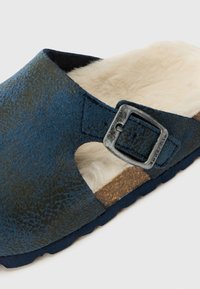 Blå och grön slip-on sandal med en texturerad ovandel, pälsfoder, korkfotbädd och silverdetalj i form av spänne. Gummiyttersula för bra grepp.