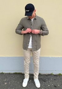 Lichtgrijze linnen overhemd, met knopen en lange mouwen. Draagt over een wit T-shirt en gecombineerd met lichtbeige jeans en witte sneakers.