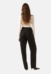 Fekete, bő szárú nadrág sima textúrával és strukturált fazonnal, magas derékkal és hátsó plissékkel, egy illeszkedő, fehér, hosszú ujjú toppal párosítva.