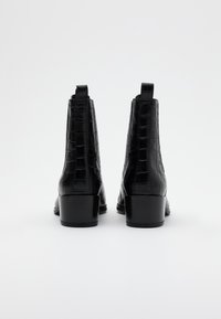 Botas de tobillo de cuero negro con textura de cocodrilo, punta redonda y tacón bajo en bloque. Presenta tiradores en la parte posterior para facilitAR el calzado.