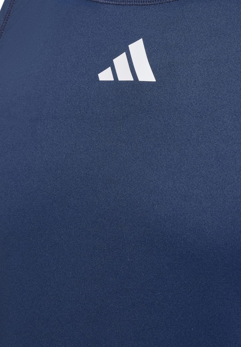 Weißes stilisiertes Dreistreifen-Logo auf der Brust eines blauen Stoffkleidungsstücks gedruckt.
