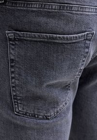 Close-up af en mørkegrå denimjeans baglomme med synlige syninger og stoftekstur.