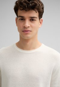 Weißer Strickpullover mit Rundhalsausschnitt, strukturiertem Stoff und gerippten Bündchen. Auffällig durch sein leichtes und atmungsaktives Design.