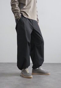 Pantaloni cargo neri, larghi e comodi, con tasche, abbinati a sneaker grigie. Il materiale sembra morbido, con un design informale e rilassato.