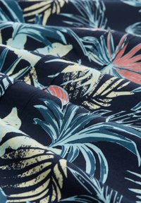 Tela floral con fondo azul marino; presenta grandes hojas de palma en tonos de teal, azul claro y coral; textura suave con colores vibrantes.