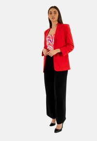 Blazer rojo sobre una blusa de rayas rosas y blancas, combinado con pantalones de pierna ancha negros y tacones altos negros. Tejido suave y ajuste a medida.
