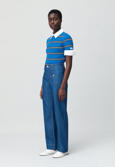 Polo en tricot rayé bleu avec col blanc, associé à un pantalon en denim bleu taille haute à jambes larges, doté de poches avant et de boutons en métal.