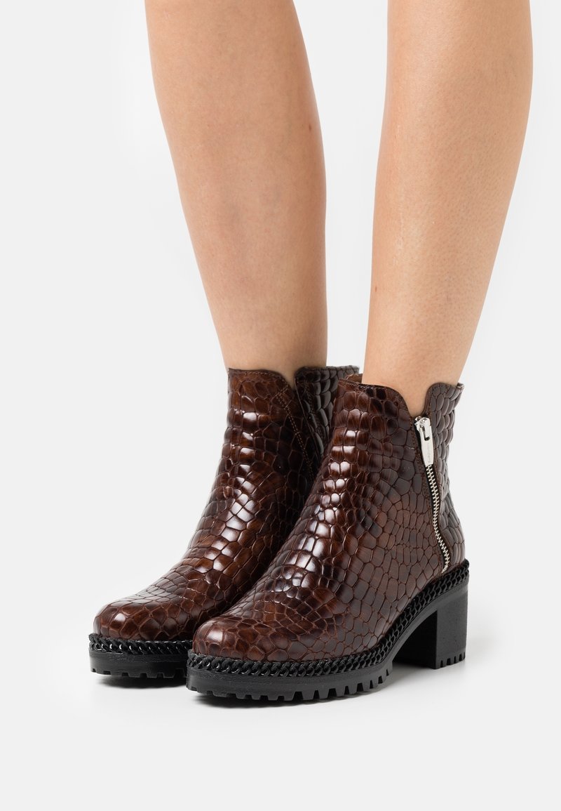 Brown crocodile-embossed ankle boots with a side zipper, black chunky sole, and textured upper. Features a low, block heel and scalloped collar.