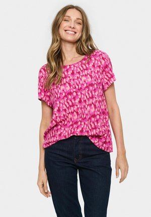 Kortærmet top i livlig pink med prikket mønster. Blødt stof, afslappet pasform og rund halsudskæring, parret med mørke jeans.