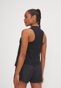 Top negro sin mangas con un diseño ajustado, hecho de material suave. Presenta un cuello alto y un dobladillo sutil, combinado con pantalones cortos negros.