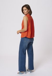 Top sans manches orange avec un dos froncé, associé à un jean évasé bleu taille haute et des sandales à talons bleu clair.