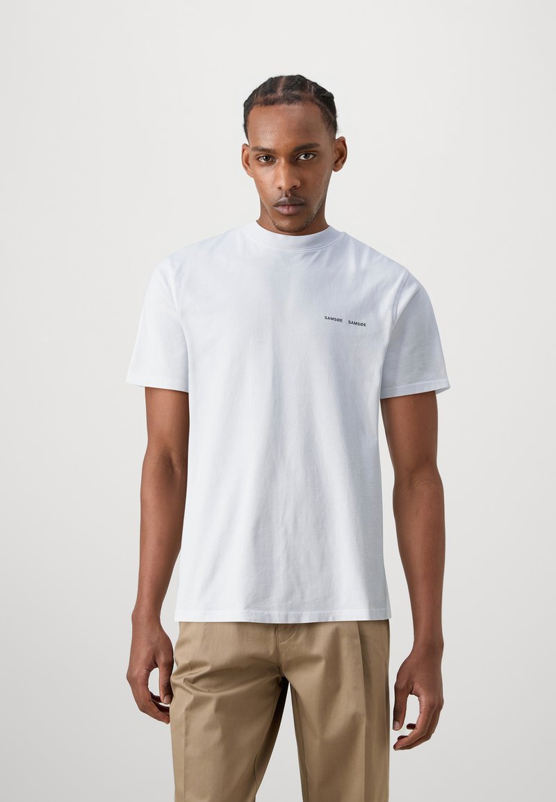 White cotton t-shirt with a crew neck and short sleeves; features subtle black text on the left chest area. Basic, unembellished design.