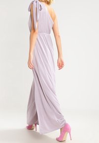 En axel lilafärgad klänning med en knuten axelrem, flödande tyg och en figurnära midja; kombinerad med rosa högklackade skor. Mjuk textur, elegant design.