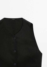 Svart ärmlös väst med V-hals, med en texturerad tyg, fem svarta knappar och en enkel, skräddarsydd design.