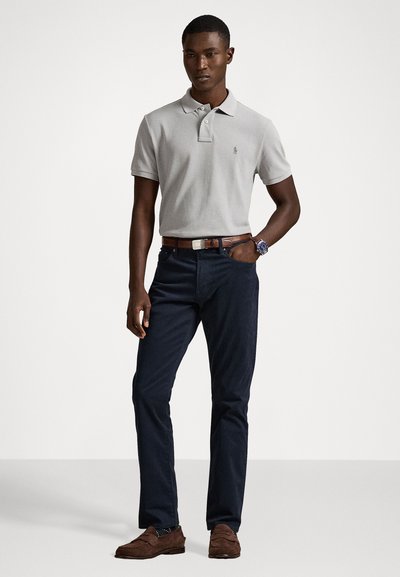 Γκρι πόλο μπλουζάκι με κοντά μανίκια, σκούρες ναυτικές παντελόνα, καφέ ζώνη και καφέ λουστρίνια. Σημαντικά χαρακτηριστικά περιλαμβάνουν ένα λογότυπο στο μπλουζάκι.