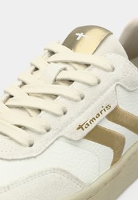 Weiße Sneaker mit strukturierter Oberseite, cremefarbenen Schnürsenkeln und goldenen Akzentstreifen. Mit Logo an der Seite und einem goldenen Einsatz auf der Zunge.