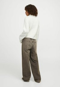 Pull en mailles crème avec une coupe décontractée et des poignets côtelés, associé à un pantalon large marron avec des poches surpiquées et une texture douce.
