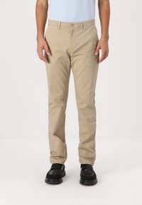 Beige bomull chinos med rett ben-design, med knappelukking og lommer. Stoffet ser glatt ut og er litt teksturert.